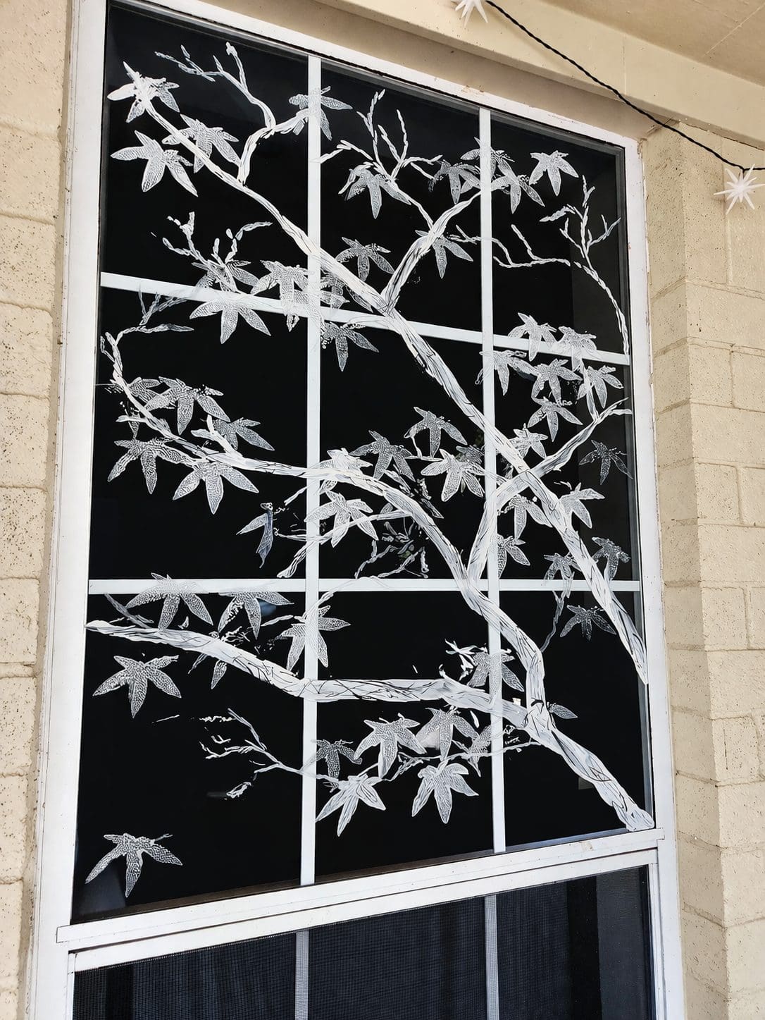 A decorative window featuring a white silhouette of a tree branch with leaves against a black background, divided into grid panes.